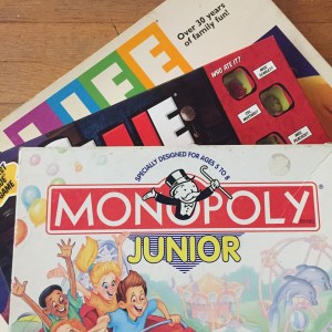 Game of Life, Clue Junior, and Monopoly Junior board games in boxes stacked one on top of another