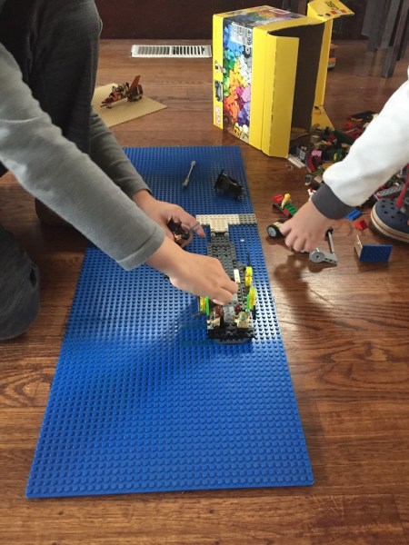 Two kids playing with Legos on big blue base plate
