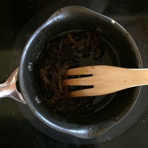 Worcestershire onion sauce in pot cooking on stove with wooden fork to stir
