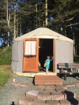 Yurt camping structure in front of woods with young child standing in open doorway
