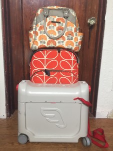 Jetkids BedBox, Orla Kiely orange stem print rollerboard suitcase, and Petunia PIcklebottom Sashay Satchel in stack of luggage