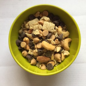 Homemade snack mix with Rice Chex cashews almonds chocolate chips peanut butter chips in small green bowl