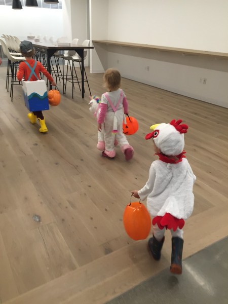 Three kids in costumes carrying orange plastic pumpkin Halloween buckets