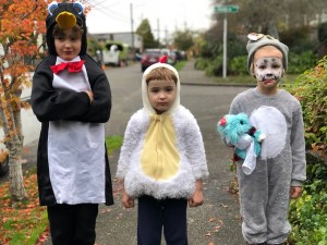 Three kids on sidewalk in Halloween costumes penguin chicken puppy dog