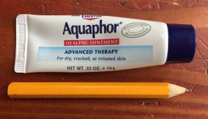Aquaphor healing ointment tiny tube on the go next to pocket pencil on hardwood floor