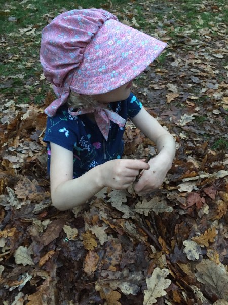Young girl in pink bonnet sitting in pile of leaves