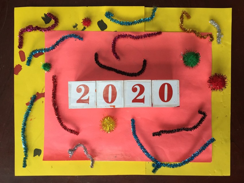 2020 year in blocks on orange and yellow background with sparkly pipe cleaners and puff balls
