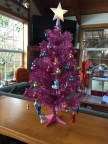 Pink miniature artificial Christmas tree with white star on top and tiny decorations