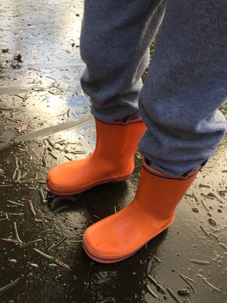 Child wearing bright orange with blue trim Norty rubber rain boots for kids