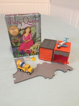 Driven tiny cars garages and road signs next to Fairy Queen card game in box on twin mattress