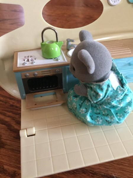 Calico Critter mouse in turquoise dress in Caravan Family Camper kitchen open oven with green teapot on top