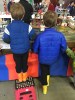 Child in blue jacket standing on Acko folding step stool at train show watching trains
