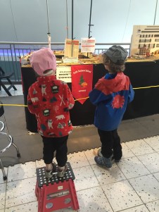 Child in red Hatley fleece jacket standing on red Acko folding step stool watching model trains on display