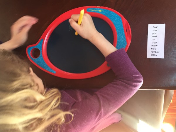 Seven year old girl practicing spelling words on Boogie drawing board at table