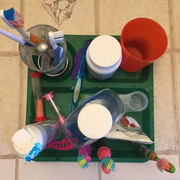 Kids' toothbrushes, mouthwash, timers, cup, and vitamins corralled on toddler divided section plate as seen from above
