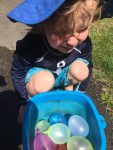 Four year old crouching next to container filled with water balloons