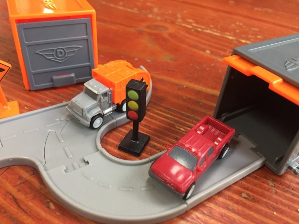 Driven Pocket series tiny trucks red pickup and orange garbage truck with small garage doors on connecting gray road pieces
