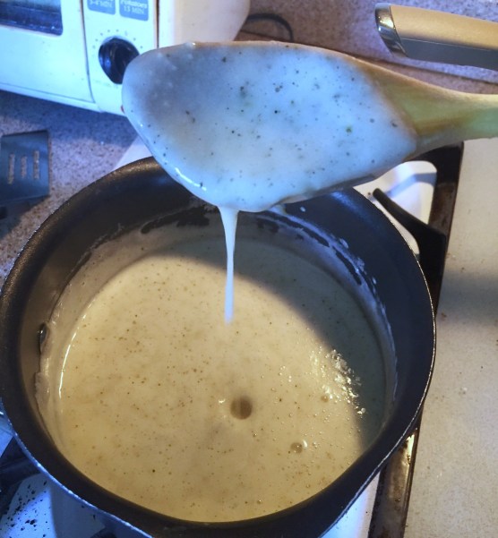 Alfredo sauce being made on stove in pot dripping from spoon
