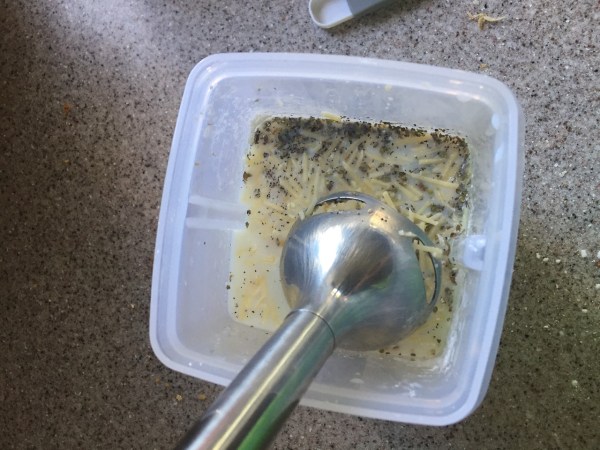 Immersion blender mixing Alfredo sauce ingredients on food container