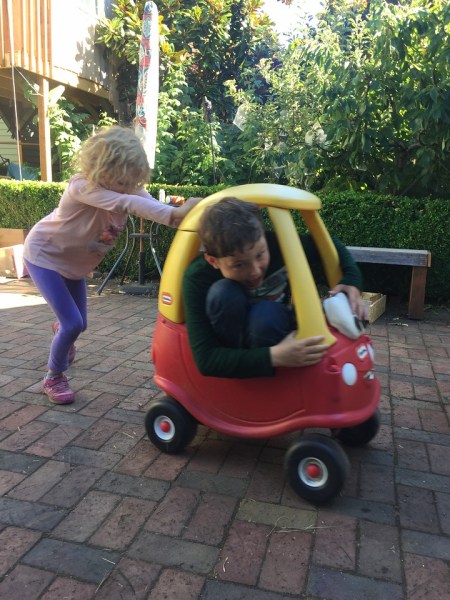 Big kids playing pushing Little Tikes Cozy Coupe red car on patio