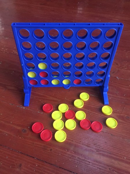 Connect 4 game in progress with red and yellow pieces dropped into blue board with holes