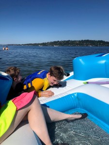 H20GO Bahama Wave Island Float on lake with legs and feet cooling in water and kids climbing back in