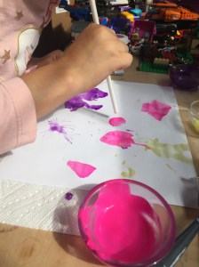 Child painting on paper by using straw to blow air to move paint