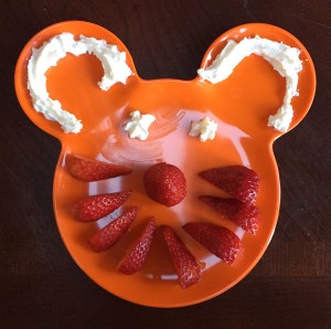 orange plastic kids Mickey Mouse shaped plate with sliced strawberries and whipped cream to make face for snack