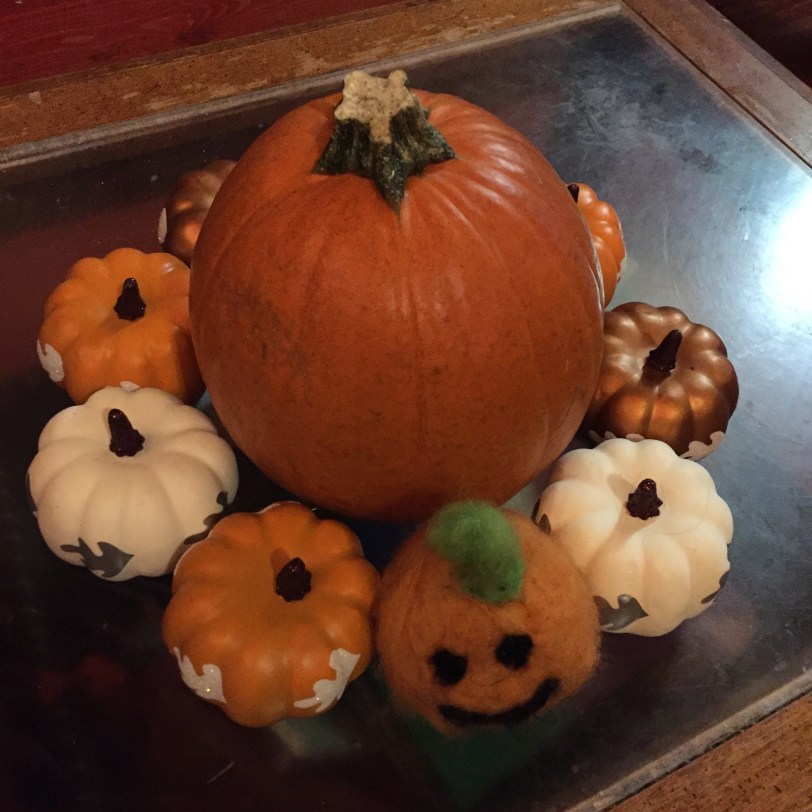 Small real pumpkin surrounded by miniature fake plastic pumpkins and one miniature homemade felted jack-o'-lantern