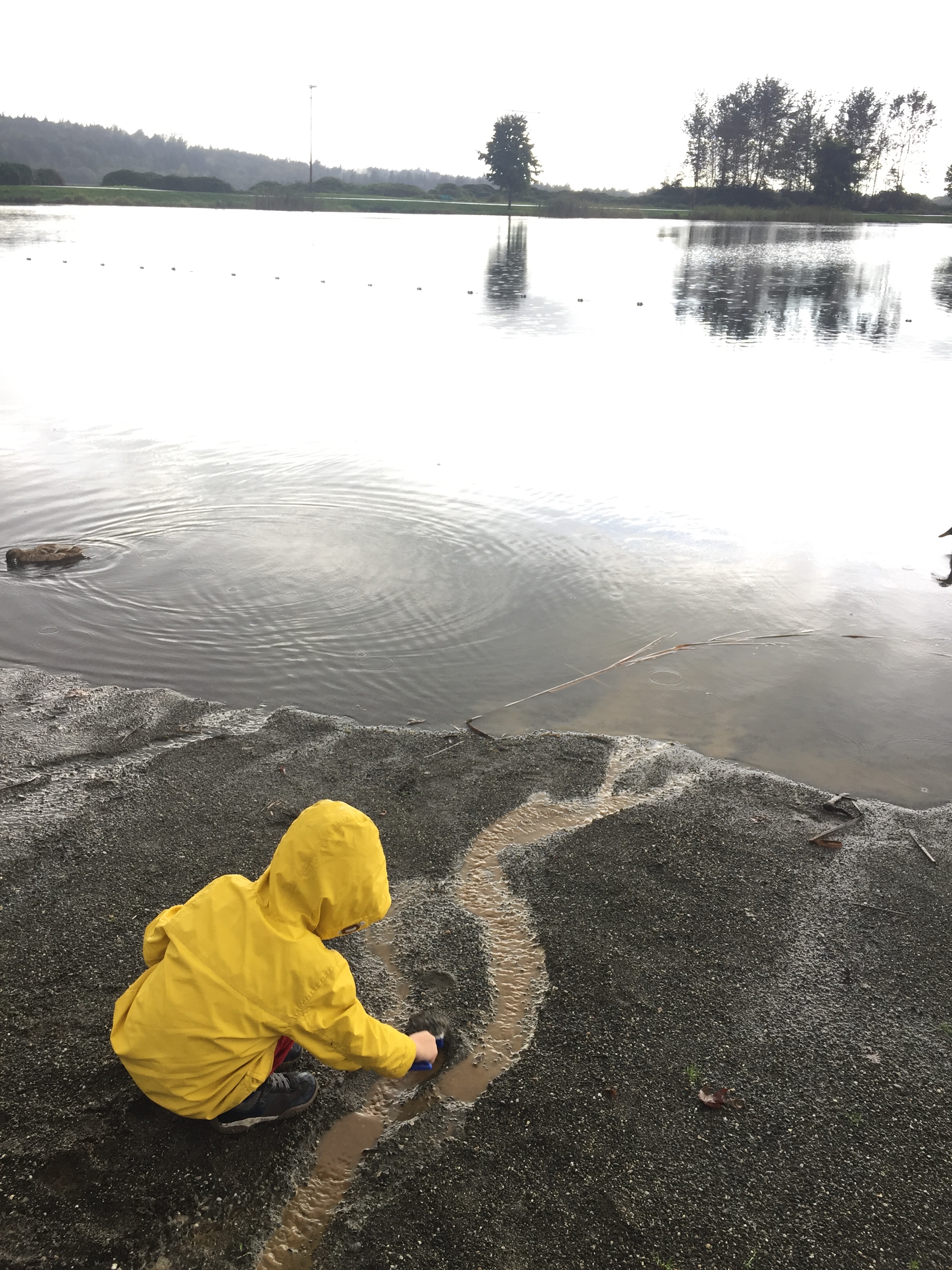 Child in raincoat digging in sand next to