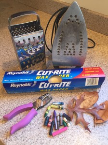Leaf sun catcher craft supplies: cheese grater, iron, wax paper, hole punch, crayon bits, leaves