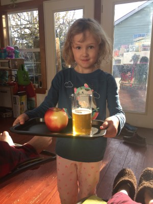 Child carrying tray with apple and drink while parents lounge inside