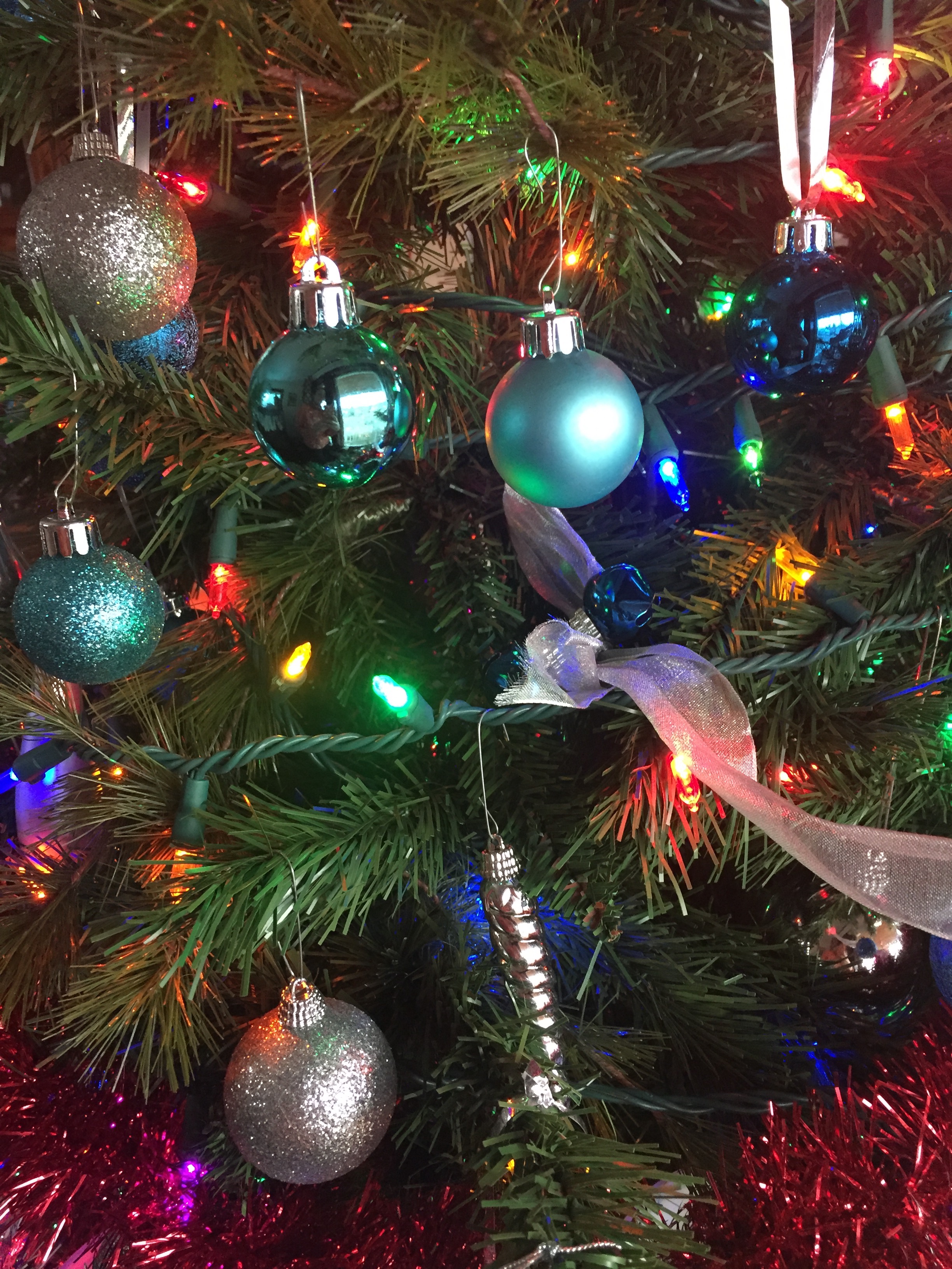 Christmas tree ornaments on tree with lights and tinsel garland