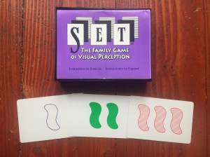 Se card game box and set of squiggles laid out one empty purple two solid green and three striped red ones