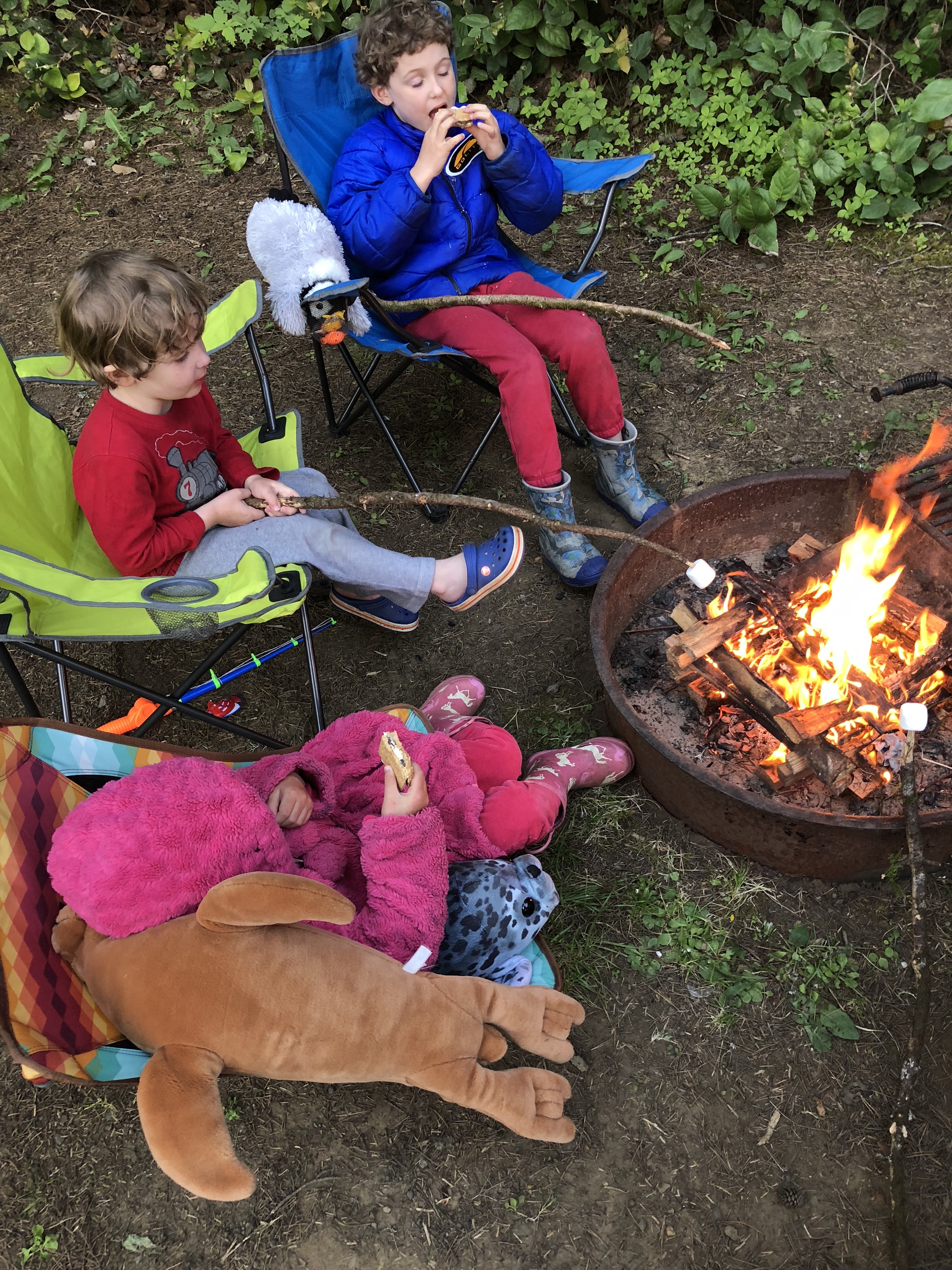 Memorial Day camping kids roasting marshmallows around campfire while sitting in camp chairs