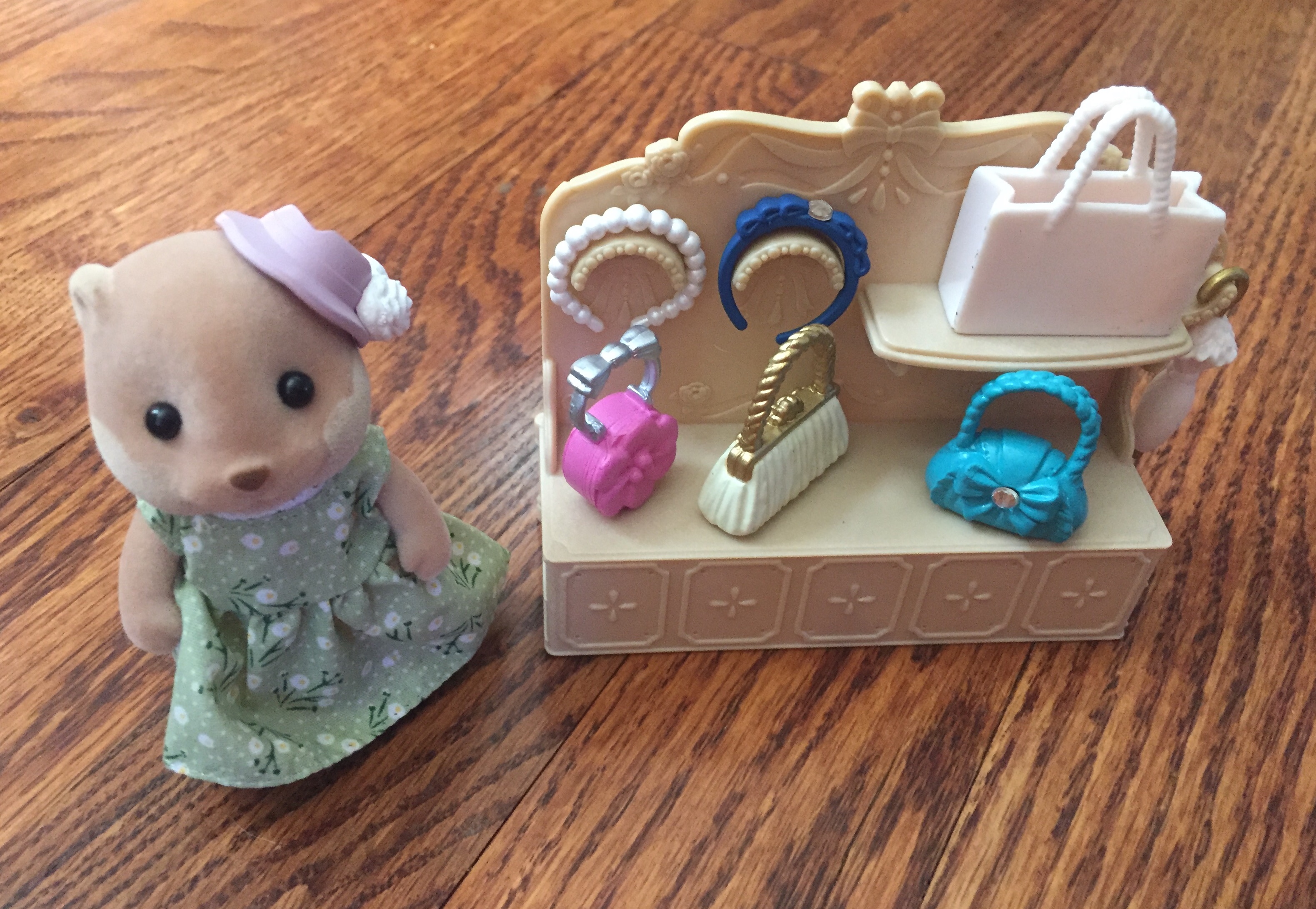 Calico Critter Otter adult wearing purple hat next to Town Fashion Showcase shelf with