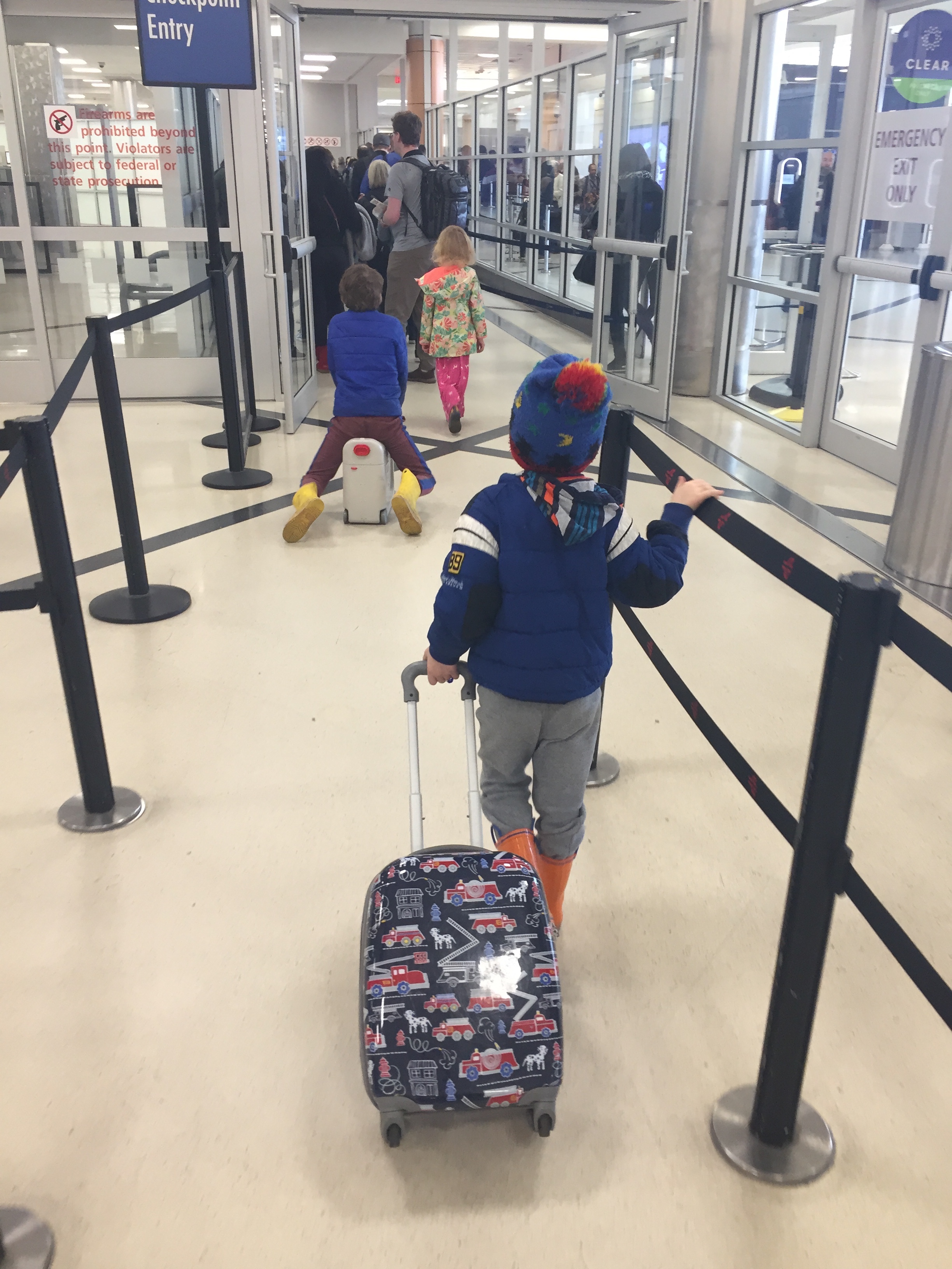 Five year old child puling Mackenzie hard-sided luggage spinner suitcase through airport security