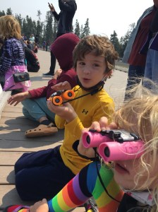 Six and nine year old child using Obuby binoculars on boardwalk at Grand Geyser in Yellowstone National Park