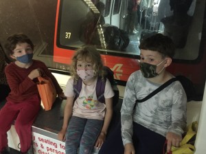 Three kids with luggage backpacks sitting on plane train