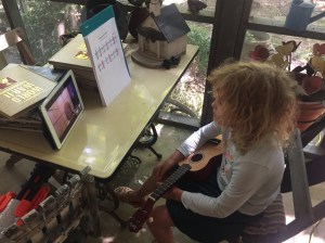 Nine year old girl playing ukulele with sheet music in front of her
