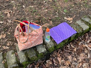 Folding purple foam camping seat sitting pad on stone wall next to bag and water bottle