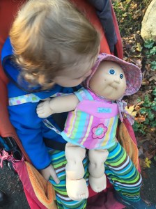 Toddler riding in stroller with Manhattan Toy Baby Stella doll carrier holding Cabbage Patch Kid doll