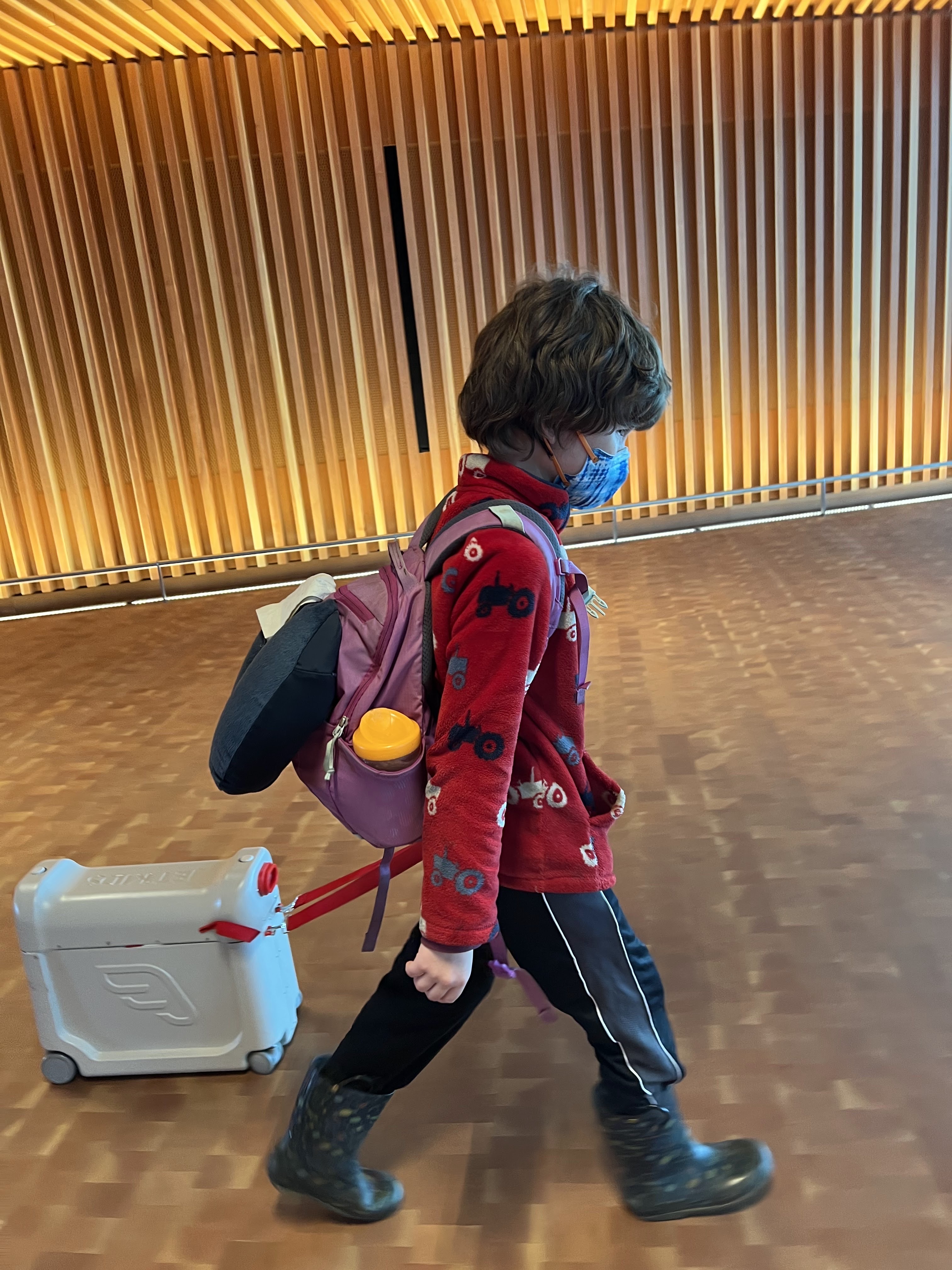Seven year old boy pulling JetKids BedBox through airport with Nuk hard spout sippy cup in backpack pocket