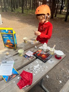 Eight year old paining plaster volcano made from National Geographic Build Your Own Volcano Kit outside on picnic table