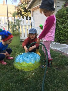 Young kids filling a batch of self sealing water balloons with hose in yard