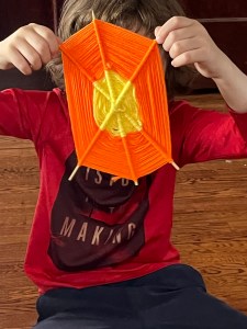 Eight year old kid holding up orange and yellow homemade god's eye web
