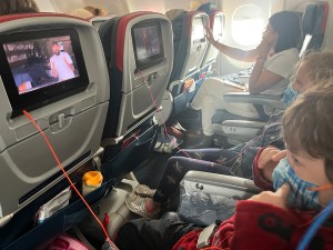 Two kids seated on airplane watching seatback entertainment