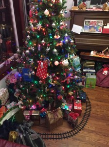 Christmas tree decorated with ornaments and lights with train track and presents underneath