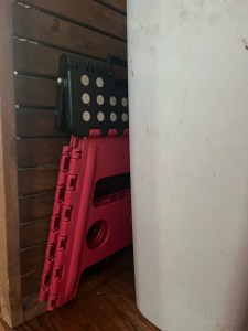 Folding step stool stored between whit recycling bin and wooden tray