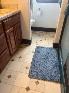 Dated bathroom design with linoleum floors, dark green shower, and wooden cabinets with beige countertops and sink